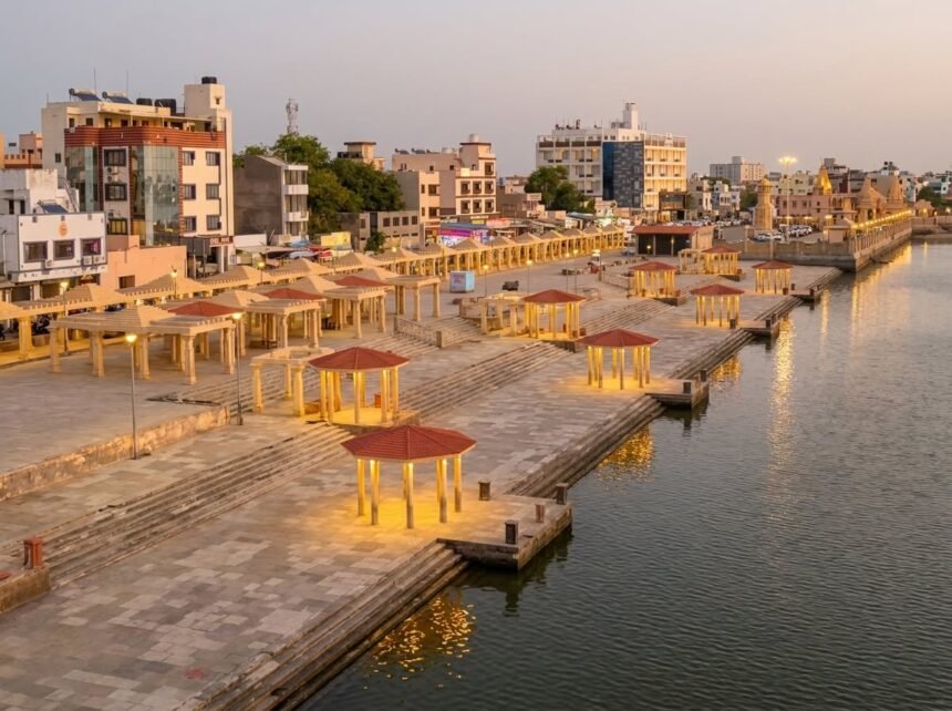 An elevated twilight view of the modern stone promenade at Gomti Ghat, featuring wide stepped terraces and rows of red-roofed pavilions glowing with warm yellow lighting alongside the calm river.